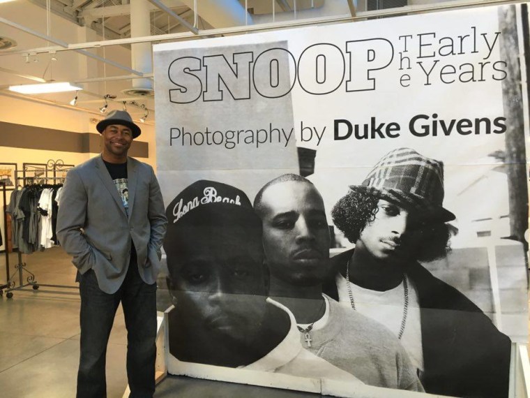 Duke givens stands next to a sign for his “SNOOP THE EARLY YEARS” exhibit
