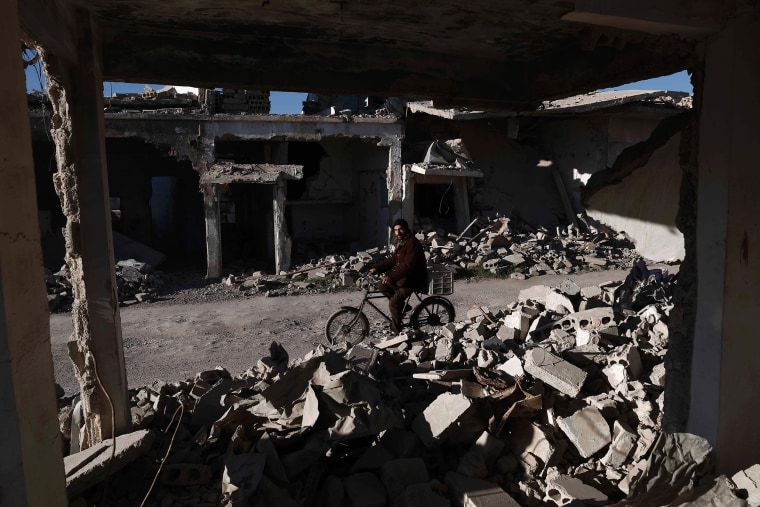 Image: A Syrian man rides his bicycle past the rubble of destroyed buildings