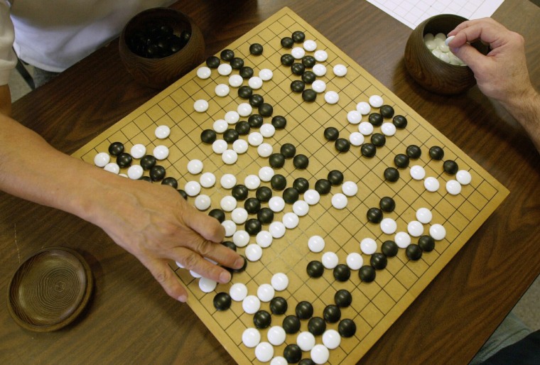 Image: A player places a black stone while his opponent waits to place a white one as they play Go