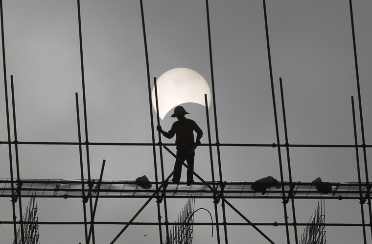 Image: A partial solar eclipse is seen as a labourer works at a construction site in Phnom Penh, Cambodia