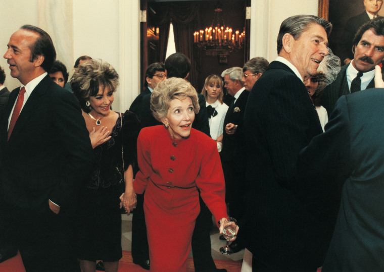 Nancy Reagan tugs on Ronald's coat as he talks with Tom Selleck with Elizabeth Taylor in tow on Jan. 20, 1985.