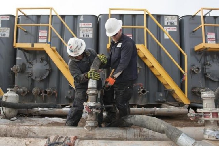 Mody Torres and Josh Anderson of Select Energy Services connect hoses between a pipeline and water tanks at a Hess site near Williston