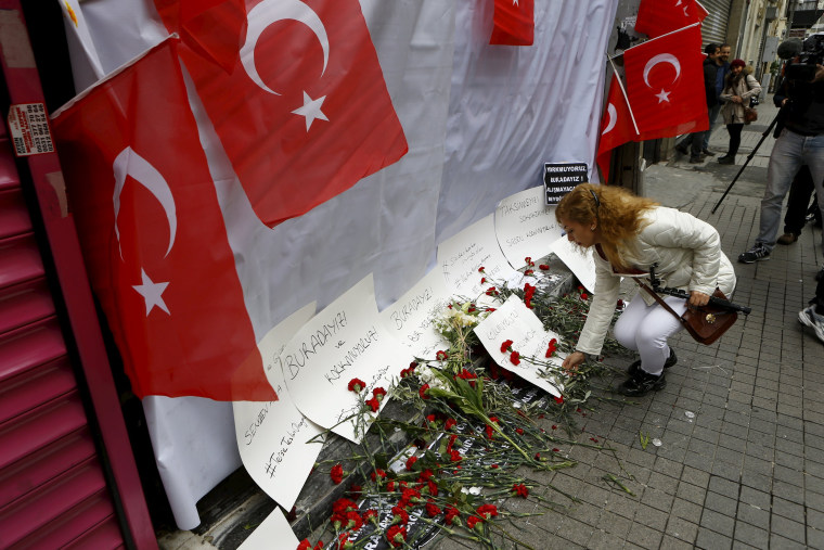 Image: A woman places carnations and a candle at the scene of a suicide bombing at Istiklal street