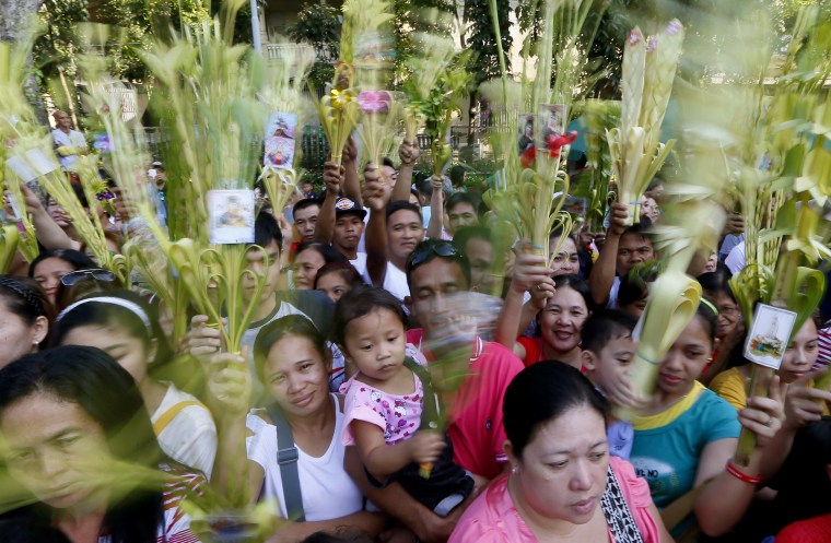 Image: Roman Catholic devotees wave palm fronds to be blessed by a priest