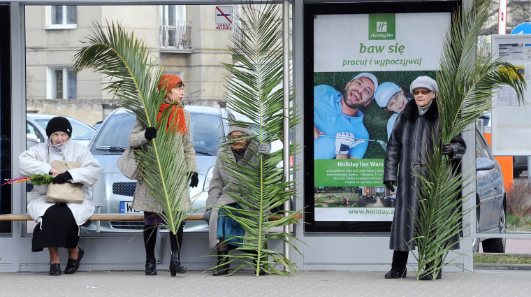 Image: Women with palm leaves wait at a bus stop after a Palm Sunday procession