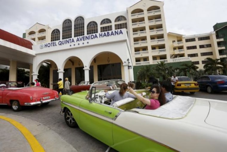 Tourists take a selfie while sitting in a vintage car outside the Quinta Avenida Habana Hotel in Havana