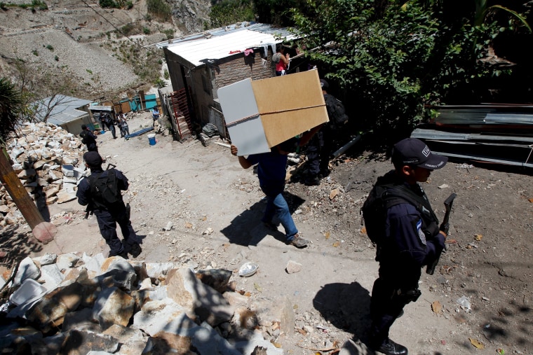 Resident carries his belongings past policemen while fleeing Las Torres neighbourhood.