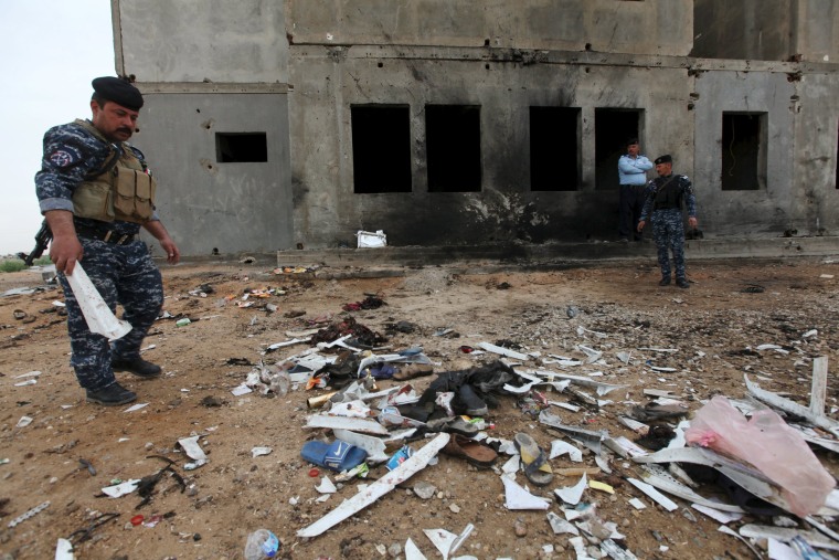 Image: Iraqi security forces inspect the aftermath of a suicide bombing at a soccer field in Iskandariya