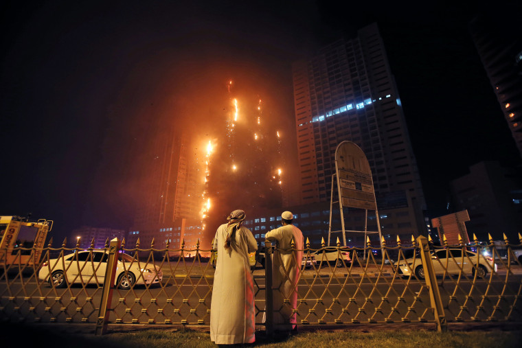 Image: Two Emirati officials watch a high-rise building as a fire spreads up the side of the building in Ajman