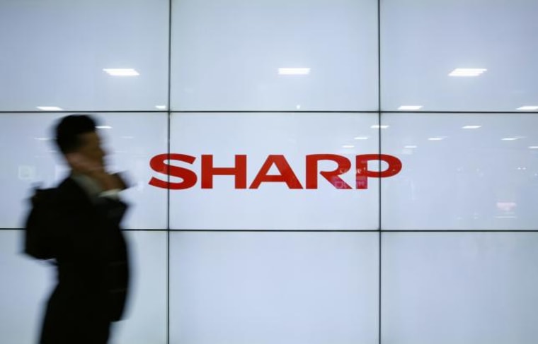 A man using his mobile phone walks past Sharp Corp's liquid crystal display monitors showing the company logo in Tokyo