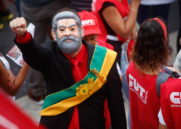 Image: A demonstrator wearing a presidential sash and a mask depicting Brazil's former President Luiz Inacio Lula da Silva attend a protest