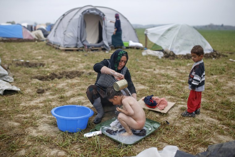 Image: A woman bathes a child at a makeshift camp for migrants and refugees at the Greek-Macedonian border near the village of Idomeni