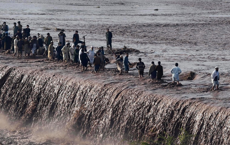 Image: Pakistani residents cross a flooded street following heavy rain