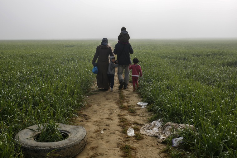 Image: A family walks through a field at a makeshift camp for migrants and refugees at the Greek-Macedonian border near the village of Idomeni
