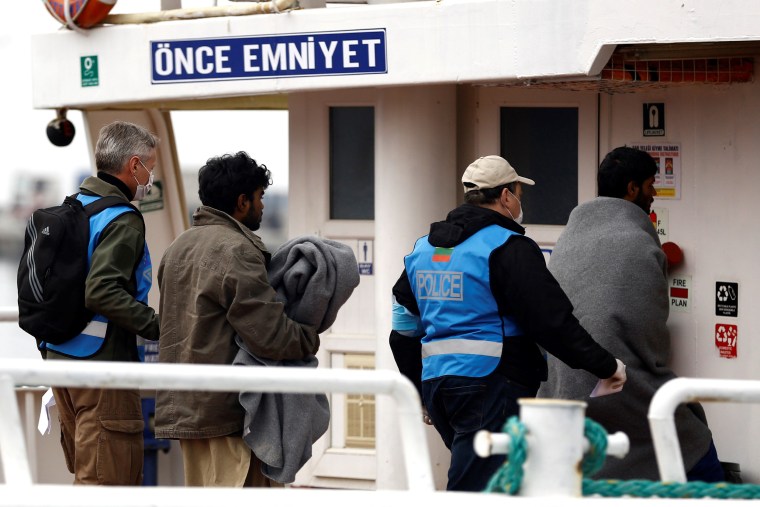 Image: A migrant is escorted onto the ferry on Friday