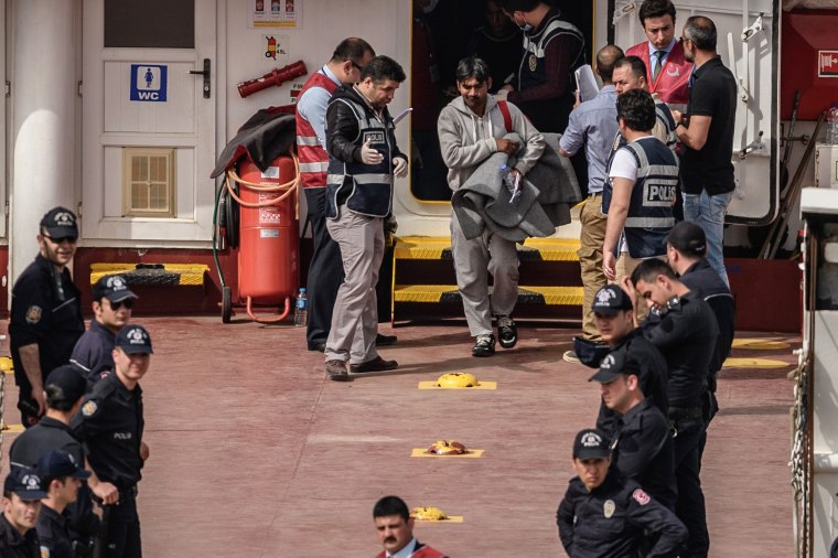 Image: A police officer escorts a migrant from a Turkish ferry