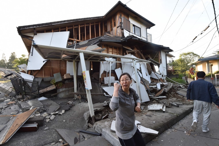 Image: A couple heads to their home past a collapsed house