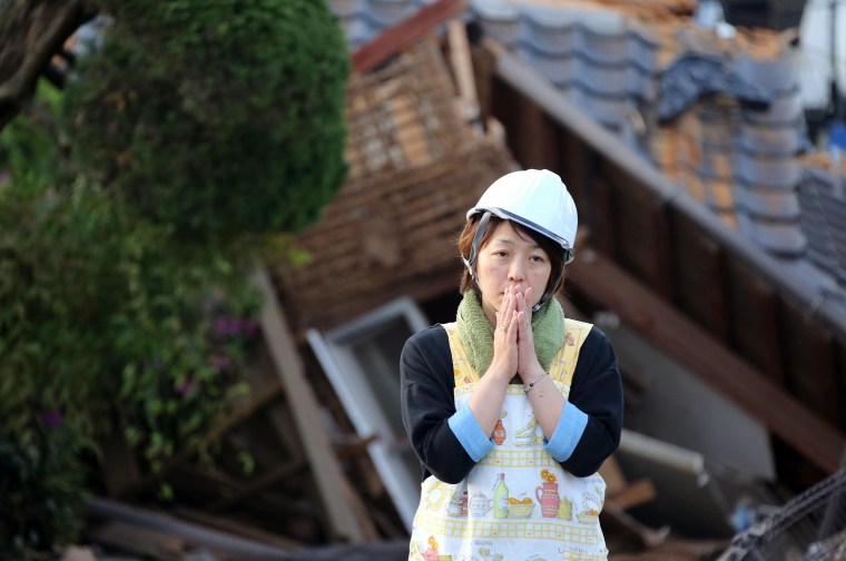 Image: A residents stands in front of a damaged house in Mashiki