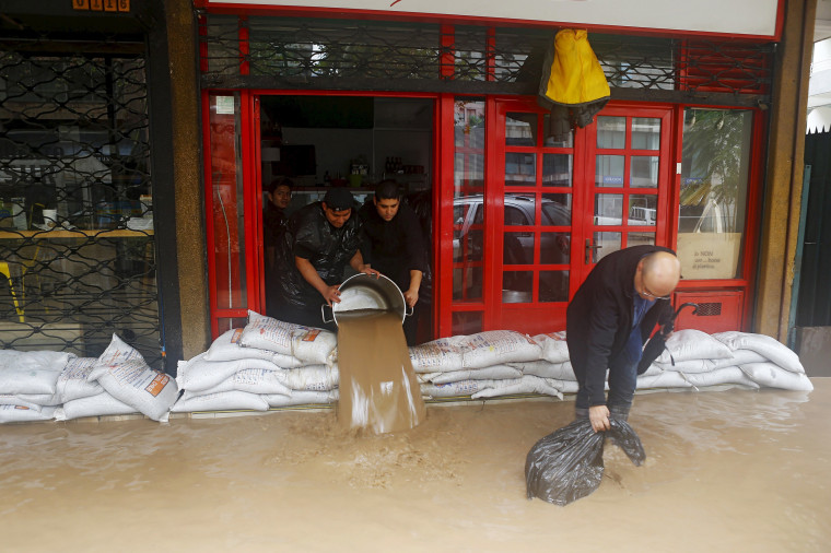 Image: Workers remove water from a store in a flooded street in Santiago