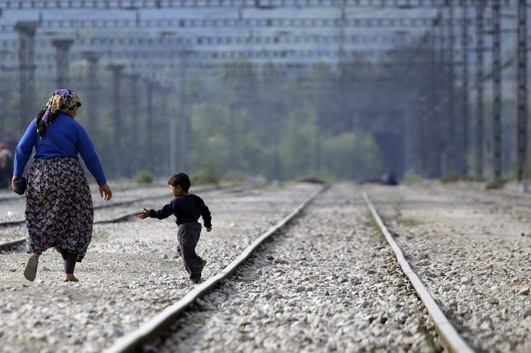 Image: A woman walks with a child along the train tracks near a makeshift camp at the northern Greek border point of Idomeni