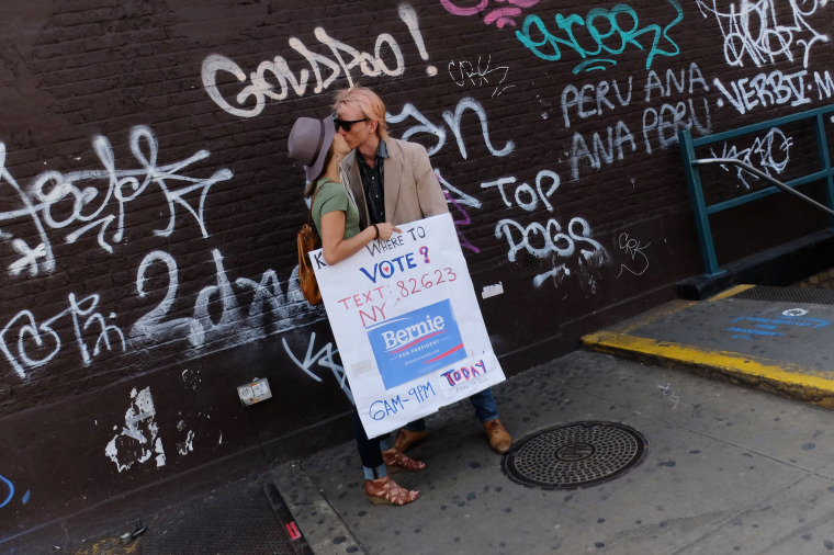 Image: A couple shares a kiss as they hold a sign to promote the vote for Bernie Sanders