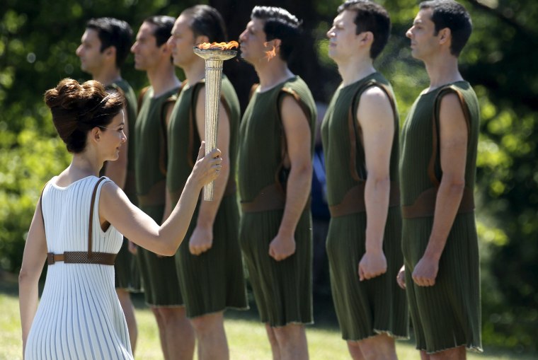 Image: Greek actress Katerina Lehou, playing the role of High Priestess, carries the Olympic flame past youths during the Olympic flame lighting ceremony
