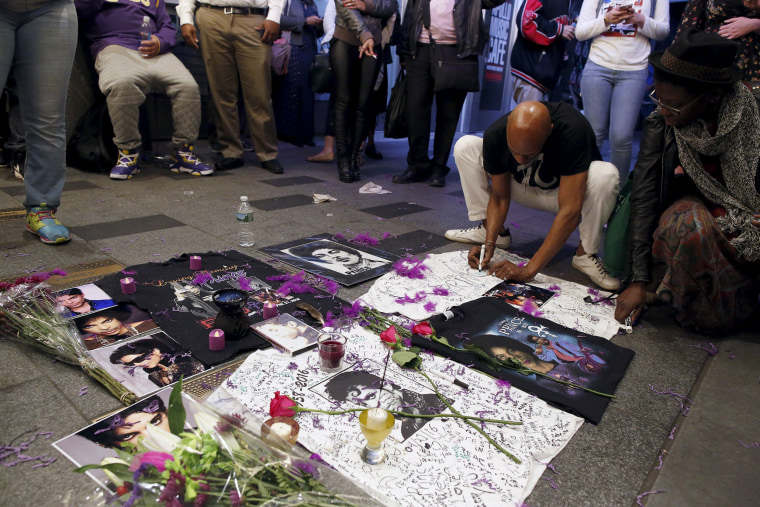 Image: A man writes on a makeshift memorial as fans gather at Harlem's Apollo Theater to celebrate the life of the deceased musician in New York