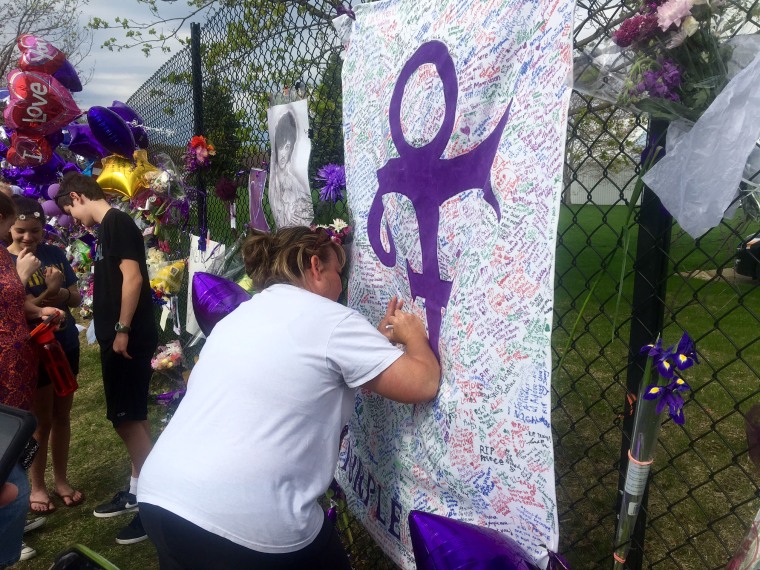 A woman writes on memorial sheet adorned with the symbol Prince once used to identify himself outside Paisley Park in Chanhassen, Minn., on April 23, 2016.