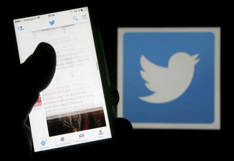 A man reads tweets on his phone in front of a displayed Twitter logo in Bordeaux, southwestern France