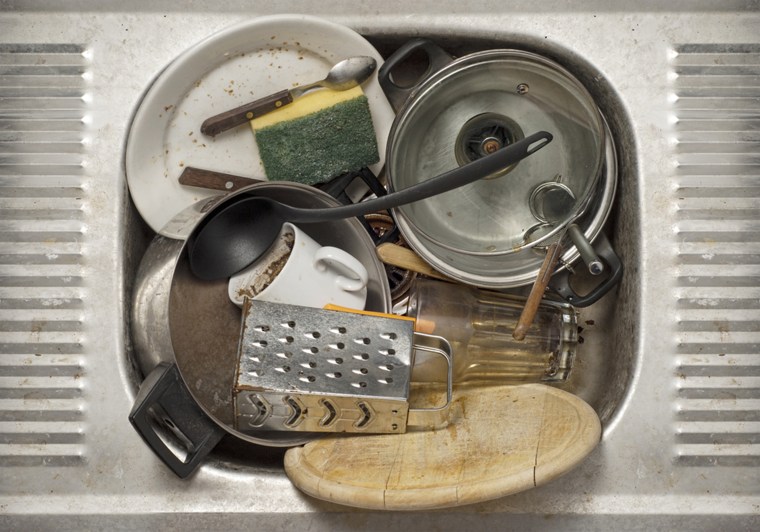 Dirty dishes, utensils in the metal sink background