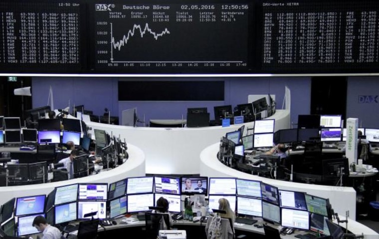 Traders work at their desks in front of the German share price index, DAX board, at the stock exchange in Frankfurt