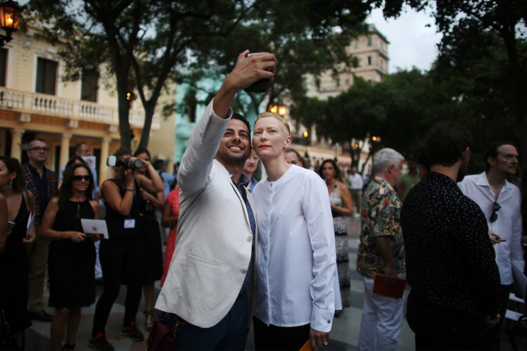 Image: Actress Tilda Swinton takes a picture with a guest prior to a fashion show displaying creations by German designer Karl Lagerfeld for fashion house Chanel at the Paseo del Prado street in Havana