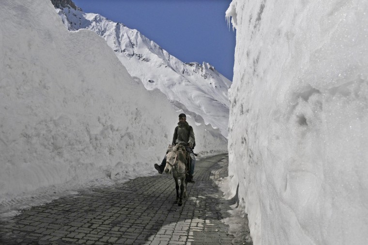 Image: A man rides a horse as he passes through a snow bound Zojila pass