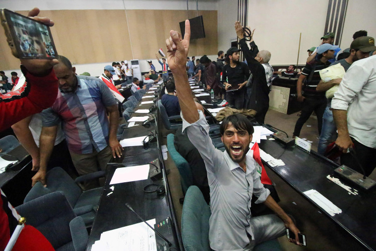 Image: Iraqi protesters shout slogans as they sit inside the parliament after breaking into Baghdad's heavily fortified Green Zone