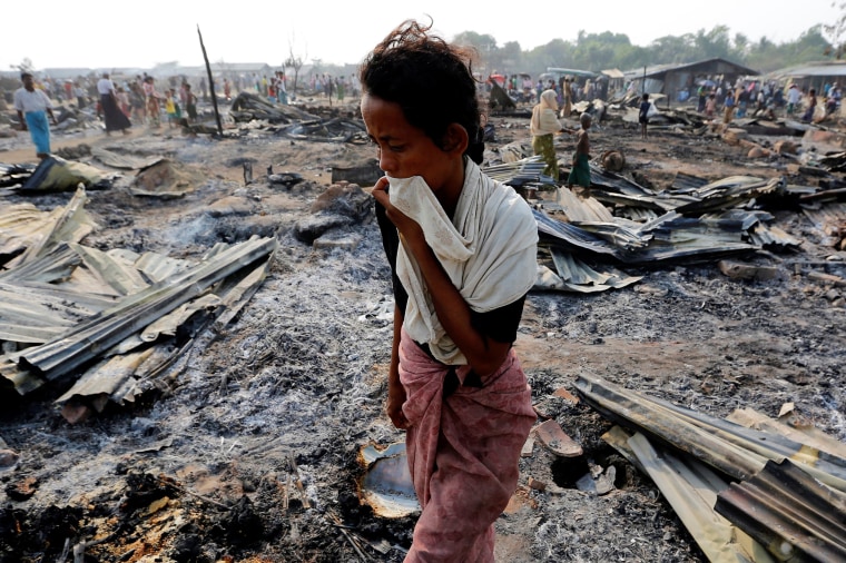 Image: A woman walks among debris after fire destroyed shelters at a camp for internally displaced Rohingya Muslims in the western Rakhine State near Sittwe