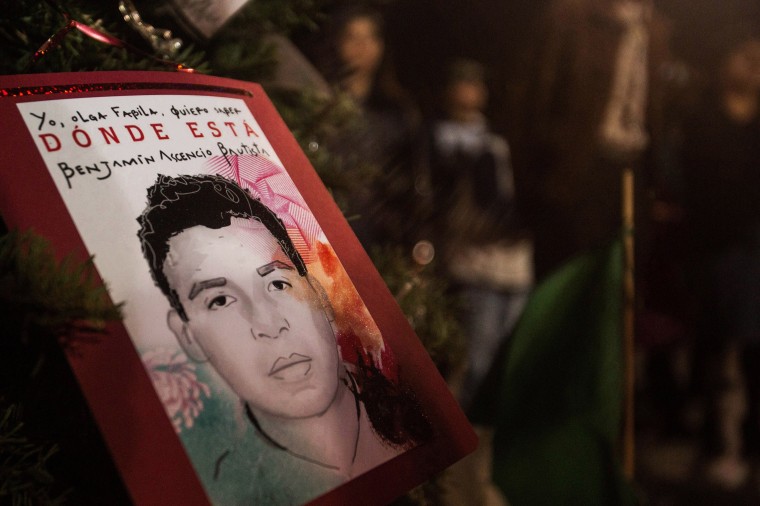 People gather around Christmas tree decorated with pictures of 43 missing students