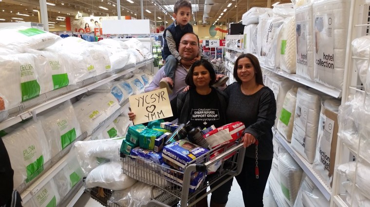 Saima Jamal, right, stands with Syrian newcomers Naser Nader and Rita Khallas as they shop for Fort McMurray evacuees. The sign they're holding up means "Syrians in Calgary love Fort McMurray."