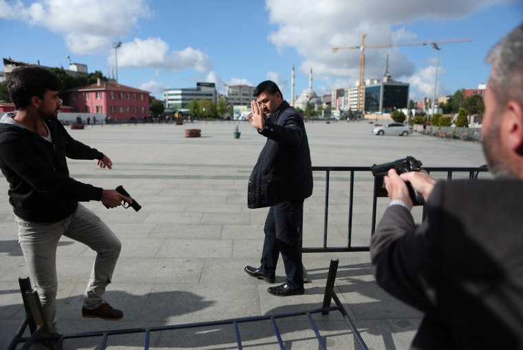 Image: Plain clothes police officers point their guns at an assailant who attempted to shoot prominent Turkish journalist Can Dundar, outside a courthouse in Istanbul