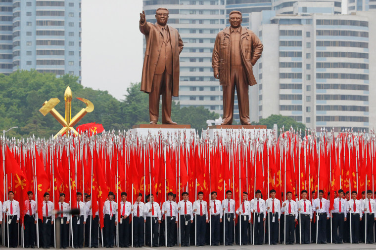 Image: Students carrying party flags stand under statues of former North Korean leaders Kim Il Sung and Kim Jong Il at the beginning of a mass rally and parade in Pyongyang
