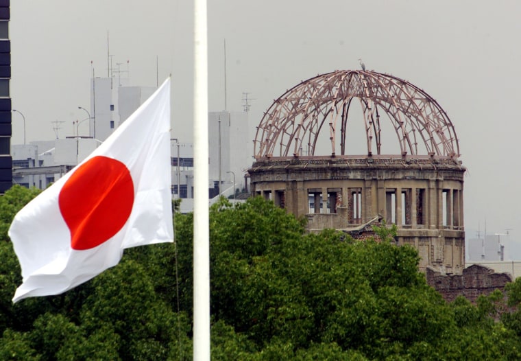Image: The Japanese national flag flutters at half-mast in the foreground of the atomic bomb dome at the Hiroshima Peace Memorial Park, in western Japan