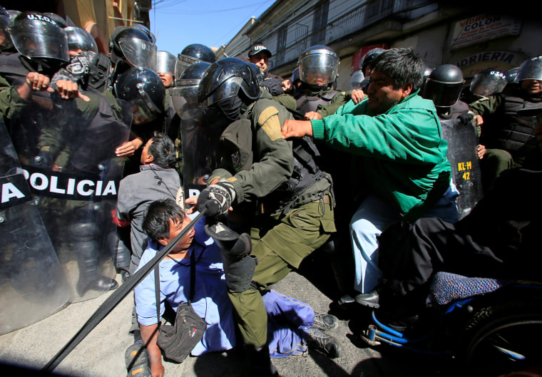 Image: Demonstrators with physical disabilities try to break through a barricade by riot police during a protest calling on the government to provide a monthly subsidy rather than an annual one in La Paz