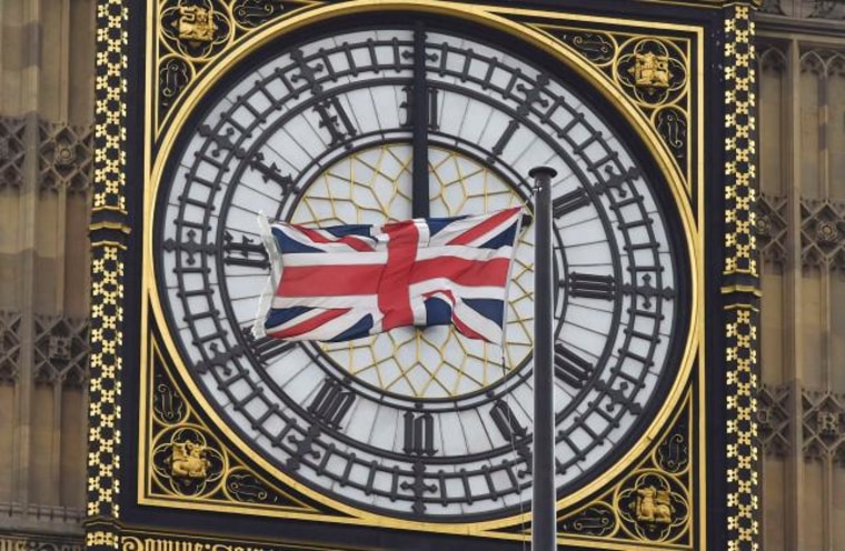 A British Union flag flutters in front of one of the clock faces of the 'Big Ben' clocktower of The Houses of Parliament in central London
