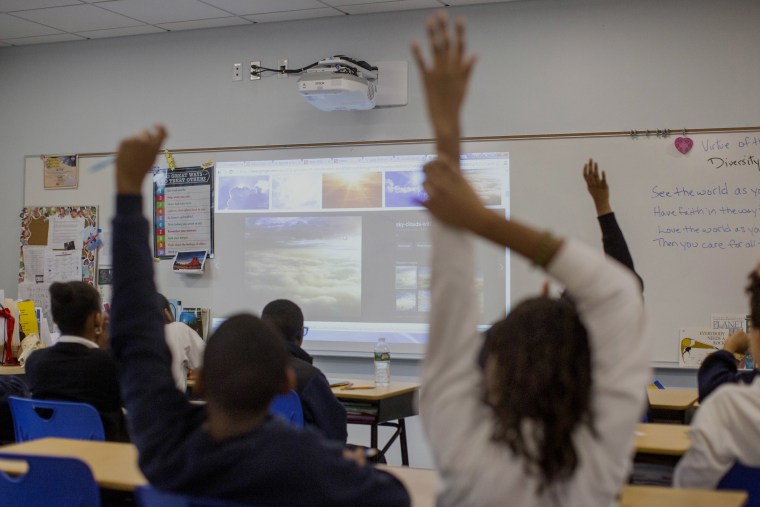 Students raise their hands in a classroom.