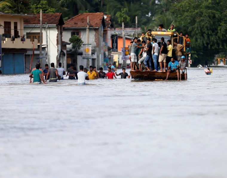 Image: People travel on a front loader as they drive through a flooded road in Biyagama