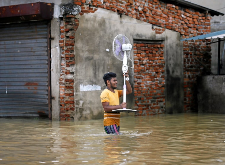 Image: A man carries a fan from his shop on a flooded road in Biyagama
