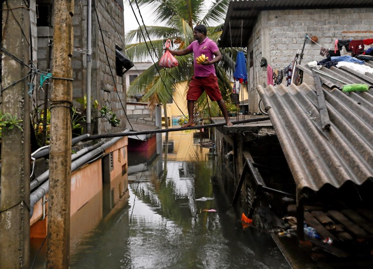 Image: A man walks on a wooden plank to hand food over to his neighbours on a flooded road in Wellampitiya