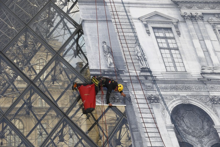 Image: Rope access technician pastes a giant picture on the Louvre Pyramid