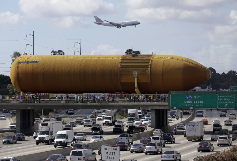 Image: A cargo plane flies overhead as the last remaining space shuttle external propellant tank is moved across the 405 freeway