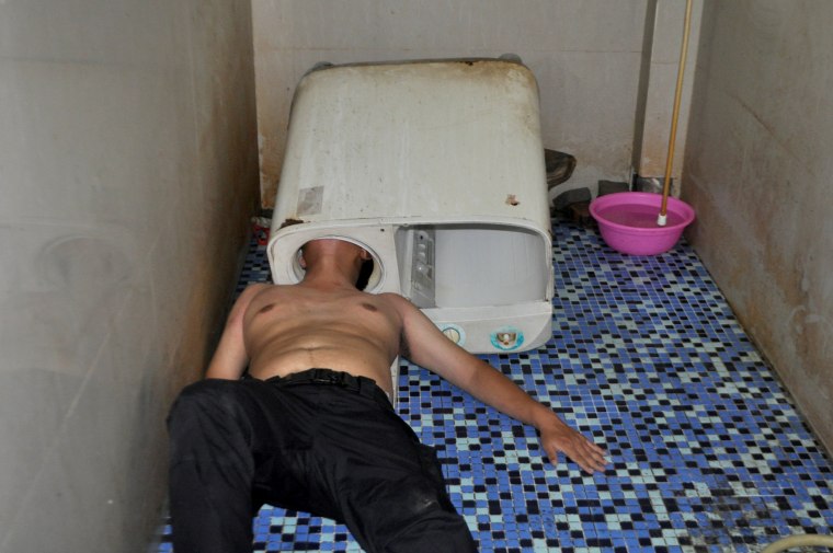 Image: A man lies on the ground as his head is stuck in a washing machine in Fuqing county of Fuzhou