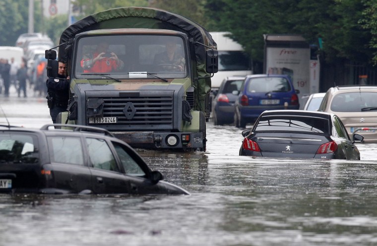 Image: A police officers hangs on a military vehicle on its way through the flooded suburb of Villeneuve-Trillage in Villeneuve Saint-Georges